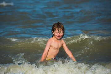 Summer kids vacation and healthy lifestyle concept. Little boy in the spray of waves at sea on a sunny day.