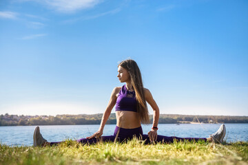 young and attractive  woman in sportswear stretching warm-up twine on  grass near the lake at daytime. Healthy lifestyle.