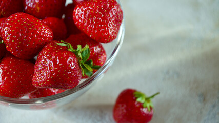 Glass bowl with ripe strawberries on a light textured background. Side view. Close-up. Copy space.