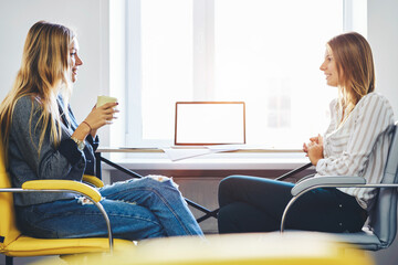 Women coworkers sitting in coworking office near computer with mock up screen