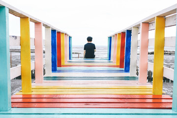 Alone traveler relax siting on colorful rainbow wooden bridge extends into the mangrove sea tourist attractions in Thailand,Active lifestyle concept.Lonely travel because of the corona virus