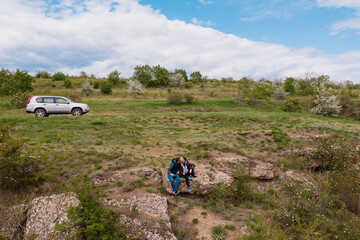Aerial view of a young couple in nature kissing and spending time together with car, rocks in the background