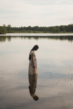 Girl in romantic dress standing in lake looking at her own reflection
