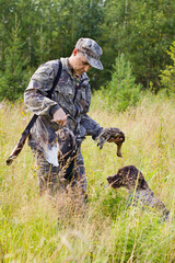 a hunter takes a downed grouse from a dog