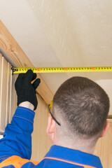 master in blue special clothes measures the width of the ceiling with a tape measure and looks at the result, close-up