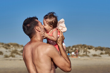 father holds her little child on hands on the beach on a sunny spring day