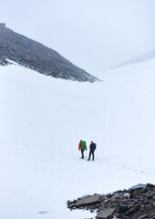 Back view of male mountaineers hiking in frozen snowy mountains. Hikers with backpacks walking through the snow and heading to mountaintop. Concept of travelling, alpinism and mountaineering.