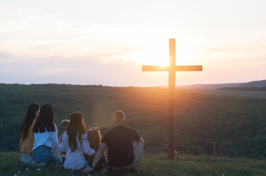 Christian family. Happy family on the nature. Children husband and wife. Wooden cross against the sky. Sunset. Summer