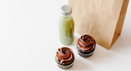 Chocolate cupcakes, green detox juice and brown paper bag on white table background. Food concept. 