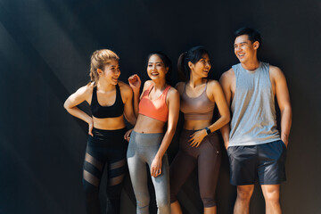 Happy smiling man and women having fun talking in gym. Group of young people relaxing in gym after workout training with black background.
