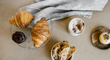 Freshly baked almond biscottis, croissants, cupcakes with cup of cappuccino background. Breakfast food concept. 