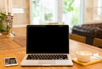 Mockup of laptop computer with empty screen with coffee cup and smartphone on table of the coffee shop background,black screen