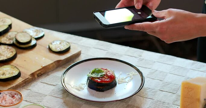 CU Woman's hands photographing egg plant slices with tomato sauce on plate with smart phone / Florence, Tuscany, Italy