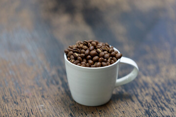 Coffee beans in white coffee cup on wood table. Close up and selective.