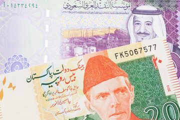An orange and green twenty Pakistani rupee bank note with a five Saudi riyal bank note in macro