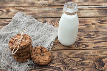 Glass of milk and chocolate chip cookies on wooden background
