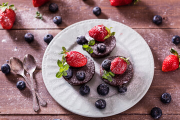 Chocolate cakes (cupcakes) are on the table. Cupcakes decorated  blueberries, strawberries and green leaves mint on top. Beautiful and elegant serving with white dishes