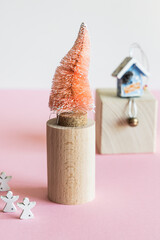 Coconut fiber orange Christmas tree on wooden stand, kraft paper gift bag on pink white background, zero waste festive concept.
