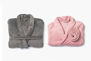 Female pink bathrobe and male gray bathrobe neatly folded lies on a white background. Copy space, flat lay