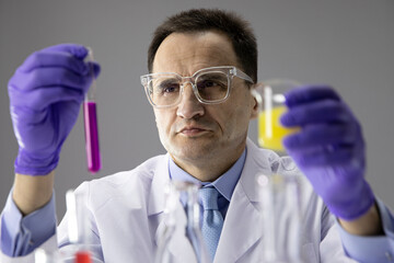 Male scientist investigator in protective goggles working at chemistry lab with reaction tubes, checking liquids in test tubes. Laboratory equipment. Scientific research, experiment, science concept