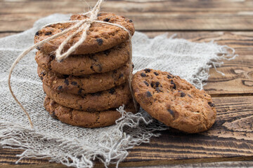 Stacked chocolate chip cookies on brown napkin. Symbolic image. Concept for a tasty snack. Sweet dessert. Rustic wooden background. Selective focus. Close up.