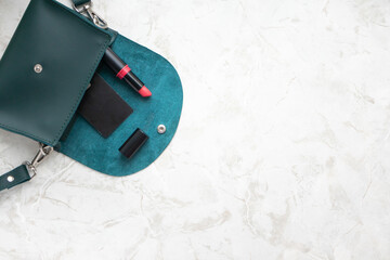 Small emerald female bag, lipstick and credit card on luxury marble table background and copy space, top view. Still life flat lay. Beauty and fashion blogging