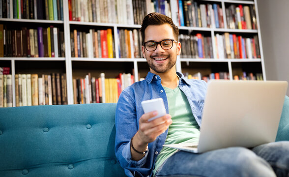 Man In Library Talking On Cell Phone And Working On Laptop