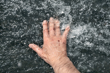 A hand dives into a stream of water. Point of view.