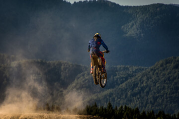 Motocross rider jumping in the air. Alps mountains in background. Dirt track on a sunny late summer...