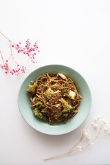 Whole grain broccoli pasta with vegetables. Presented in green plate surrounded with flowers.