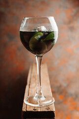 Black cocktail with lime slices in wine glass on the rustic background. Selective focus. Shallow depth of field. 