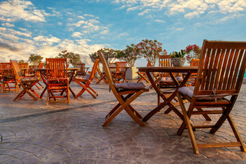 Outdoor terrace of a cafe with empty wooden chairs and tables on a background of blue sunset sky