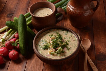 Russian cuisine- Okroshka, Summer light cold yogurt soup with cucumber, radish, eggs and dill with sour cream  and green onion on a  wooden table.  