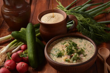 Russian cuisine- Okroshka, Summer light cold yogurt soup with cucumber, radish, eggs and dill with sour cream  and green onion on a  wooden table.  