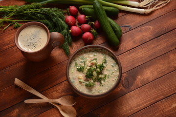 Russian cuisine- Okroshka, Summer light cold yogurt soup with cucumber, radish, eggs and dill with sour cream  and green onion on a  wooden table.  