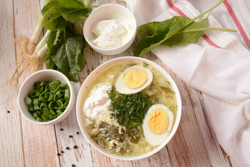 Green sorrel and spinach soup with boiled egg, spring onion and sour cream on white wooden rustic table. Diet or healthy food concept