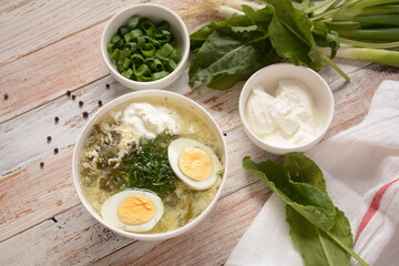 Green sorrel and spinach soup with boiled egg, spring onion and sour cream on white wooden rustic table. Diet or healthy food concept