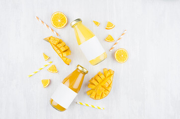 Fresh yellow orange juice and mango juice in glass bottles with blank label, ingredients on white...