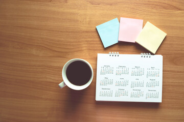 Travel Planning on Calendar and use post-it for note with a cup of coffee on a wooden table