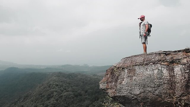 Backpacker with valley view. Hiker man comes to the edge of the mountain and then lied down to the ground with backpack using as a pillow