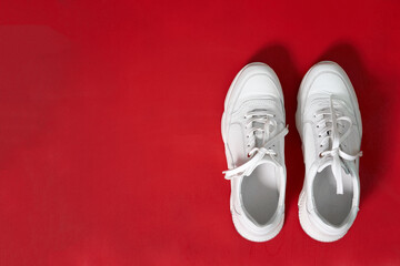 Fashion concept. New women's white stylish leather sneakers on red wall background. Thick-soled sneakers.