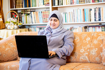 Happy arabic muslim woman sitting on couch alone using technology