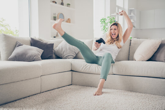 Photo of beautiful cheerful funny lady sit comfy couch raise fist leg positive emotions playing video games stay home quarantine excited addicted gamer winner victory living room indoors