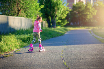 A little girl rides on pink roller skates on asphalt in the summer. The child learns to ride roller skates. Skating