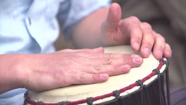 Musician playing rhythmic percussion drums with his hands on a sunny day in slow motion close up shot