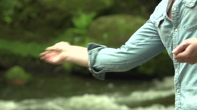 Man throw a stone pebble in the water in nature in the  forest with water and stones in the background in slow motion close up shot