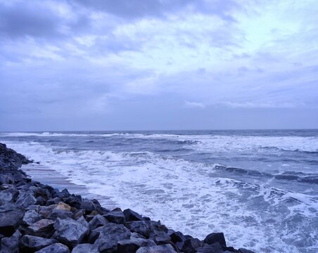 A picture of beach with rocks on the shore and cloudy sky on background. The sea is violent with strong waves in this picture. Kappil Beach (Varkala Town), Kerala.