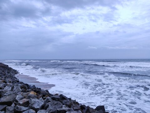 A picture of beach with rocks on the shore and cloudy sky on background. The sea is violent with strong waves in this picture. Kappil Beach (Varkala Town), Kerala.