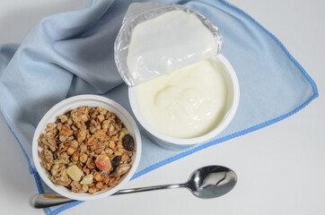 Open can of yogurt to add granola, with a dessert spoon on a blue soft cloth background.