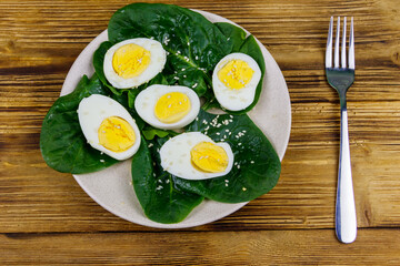 Boiled eggs with fresh spinach leaves and sesame seeds on wooden table. Top view